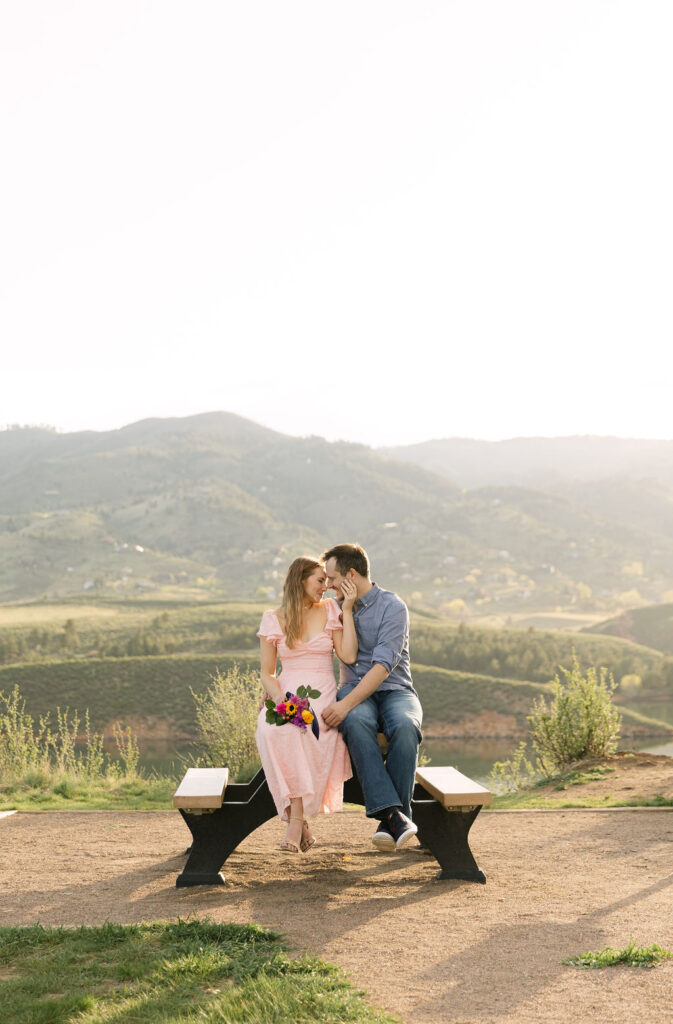 Couple sitting together on a bench overlooking Horsetooth Reservoir during their summer engagement session