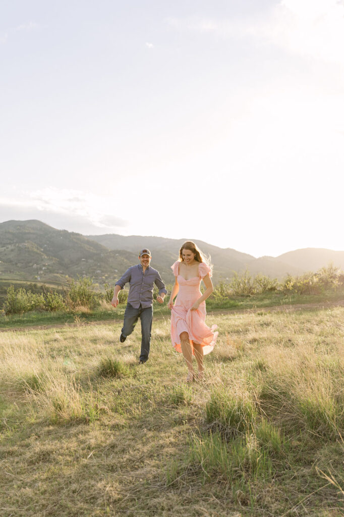 Couple running through the tall grass at Horsetooth Reservoir during golden hour.
