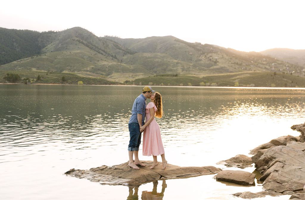 Couple holding hands and walking barefoot on the rocks at the lake’s edge.