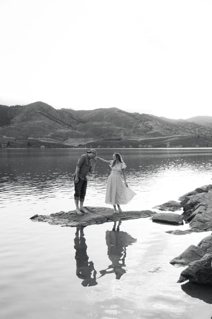 Black and white photo of the couple standing on the rocks at Horsetooth Reservoir with their reflection in the water.