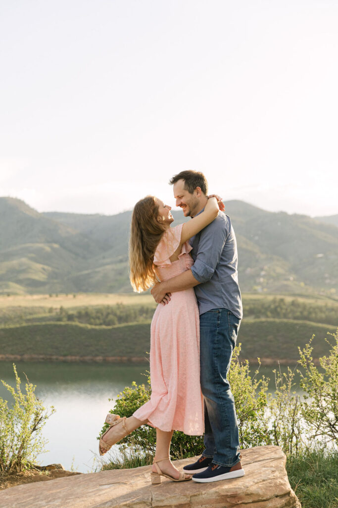 Couple embracing on a rock overlooking Horsetooth Reservoir at sunset.