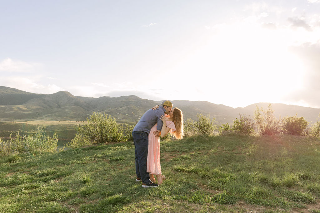 Ross dipping Annelise for a kiss with the foothills behind them during their sunset engagement photos in Colorado.