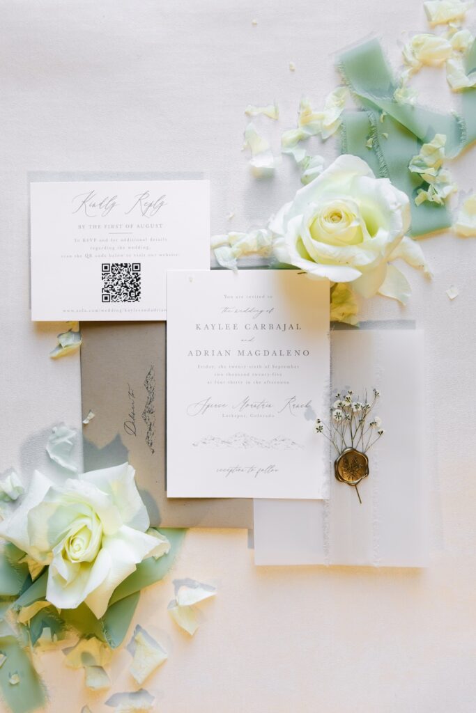 Luxury flatlay of wedding invitations with white roses and soft green florals for a Spruce Mountain Ranch wedding.