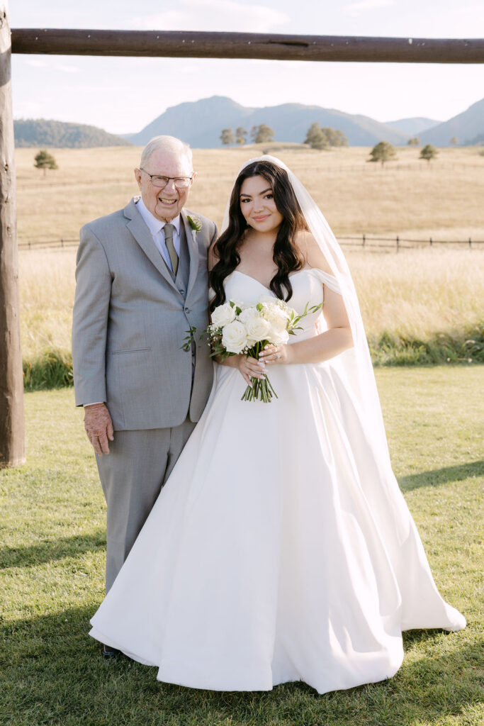 Bride and grandfather standing under wooden arch at Spruce Mountain Ranch.