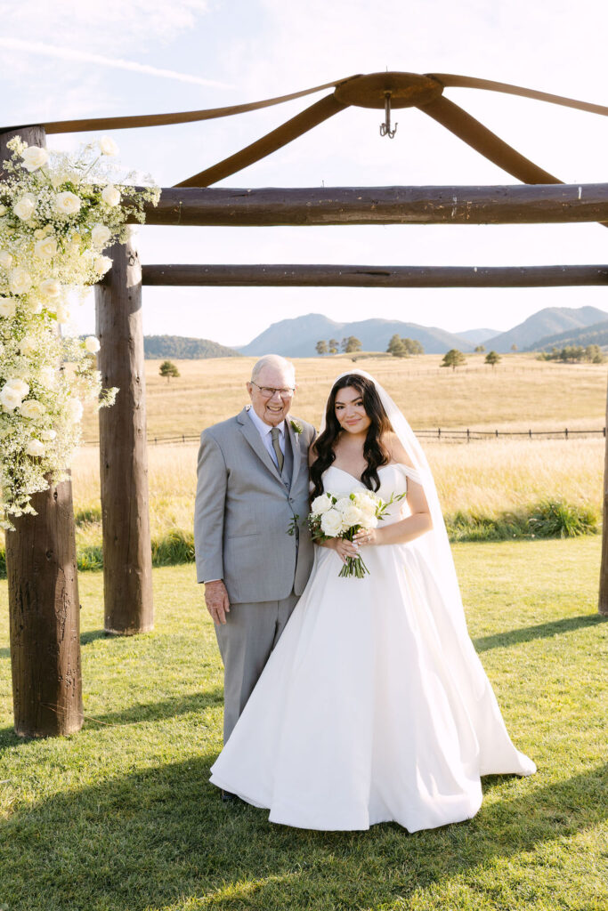 Bride and father standing under wooden arch at Spruce Mountain Ranch.