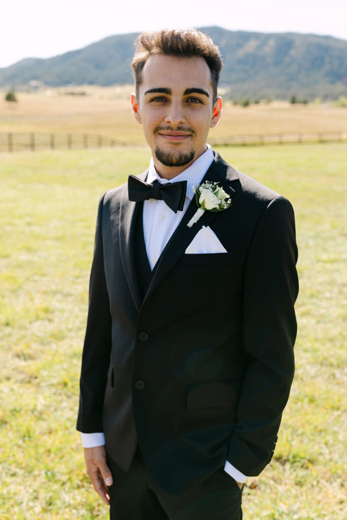 Groom portrait in black tuxedo with mountain views behind him.