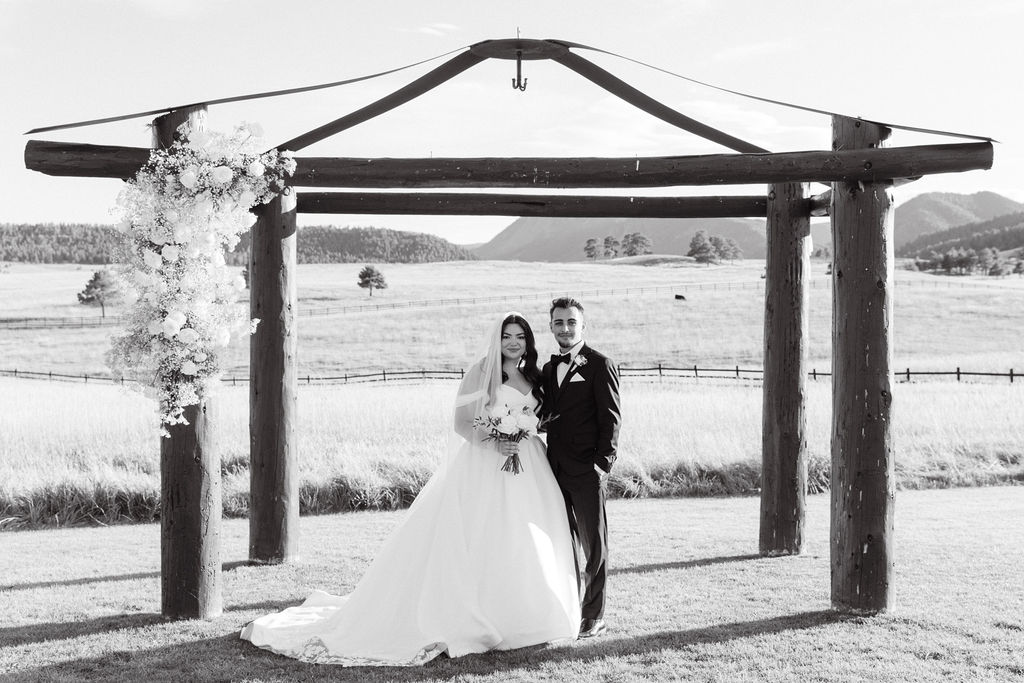 Black and white portrait of bride and groom under the wooden ceremony arch at Spruce Mountain Ranch.