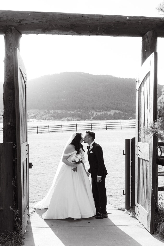 Bride and groom standing in barn doorway overlooking the Colorado mountains.