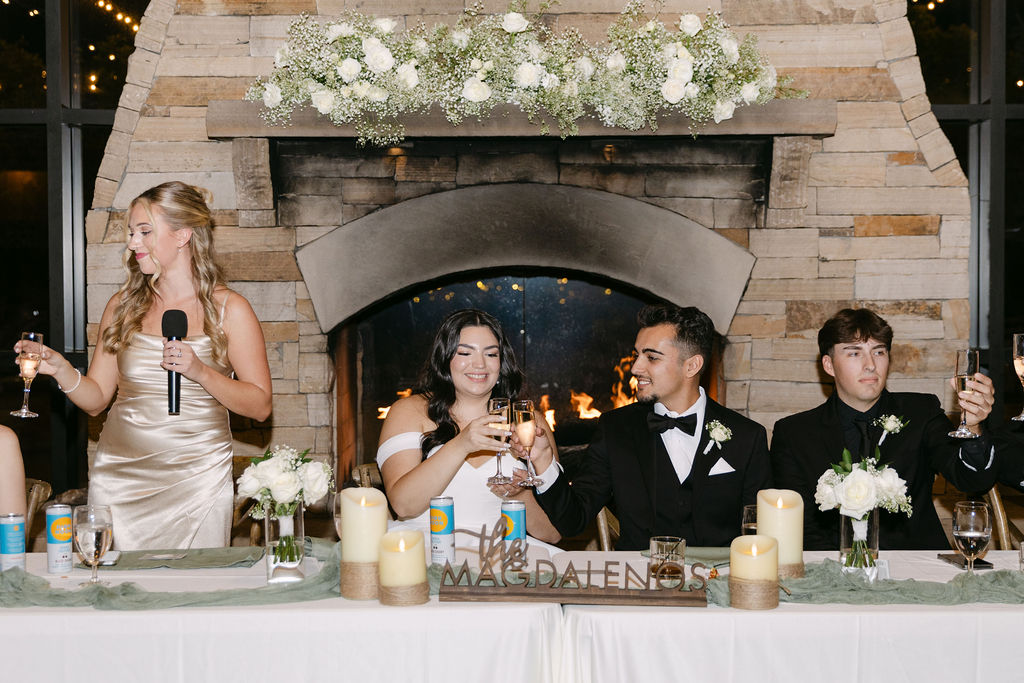 Wedding party seated at the head table inside the lodge reception space.