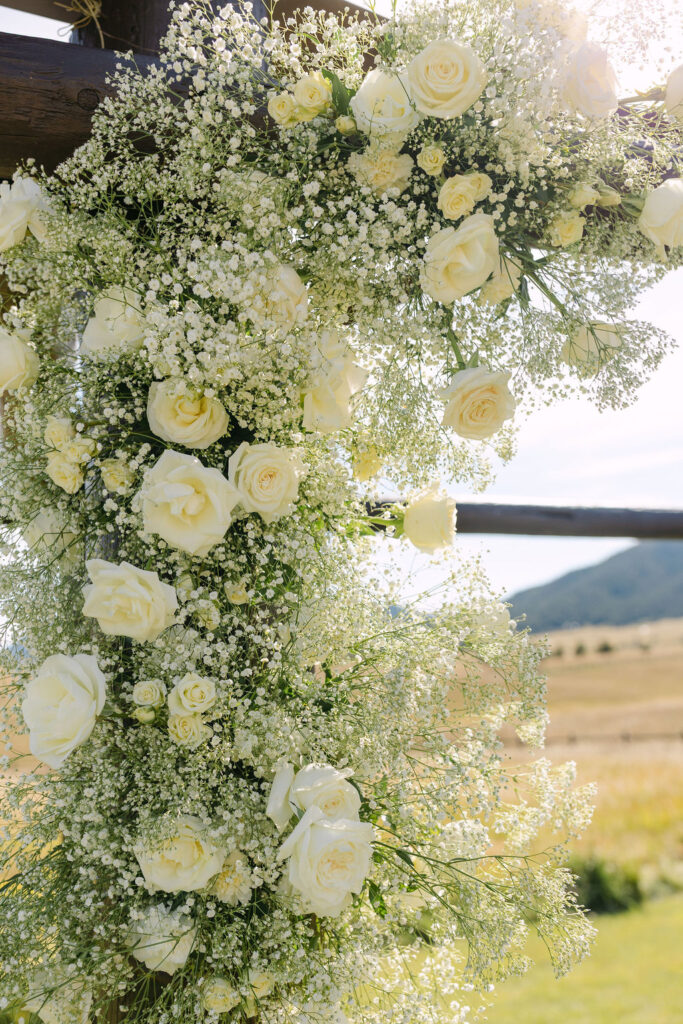 Close-up of lush white floral ceremony arch installation with roses and baby’s breath.