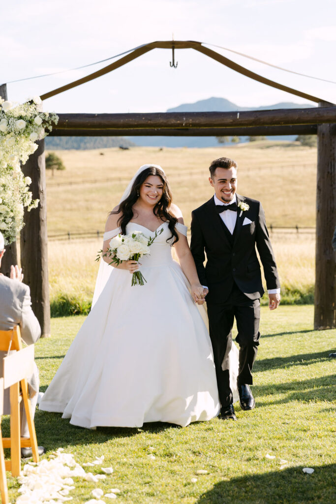 Bride and groom recessing down the aisle smiling at Spruce Mountain Ranch.