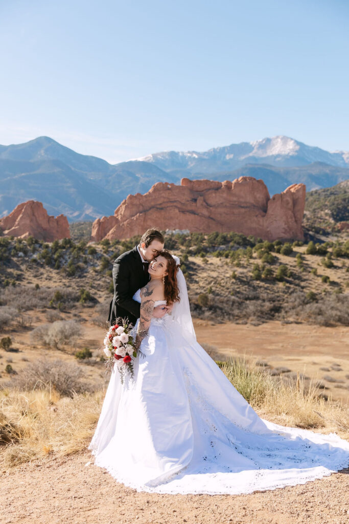 Groom embracing his bride as her long train is spread out in Garden of the gods for a classic wedding photo 