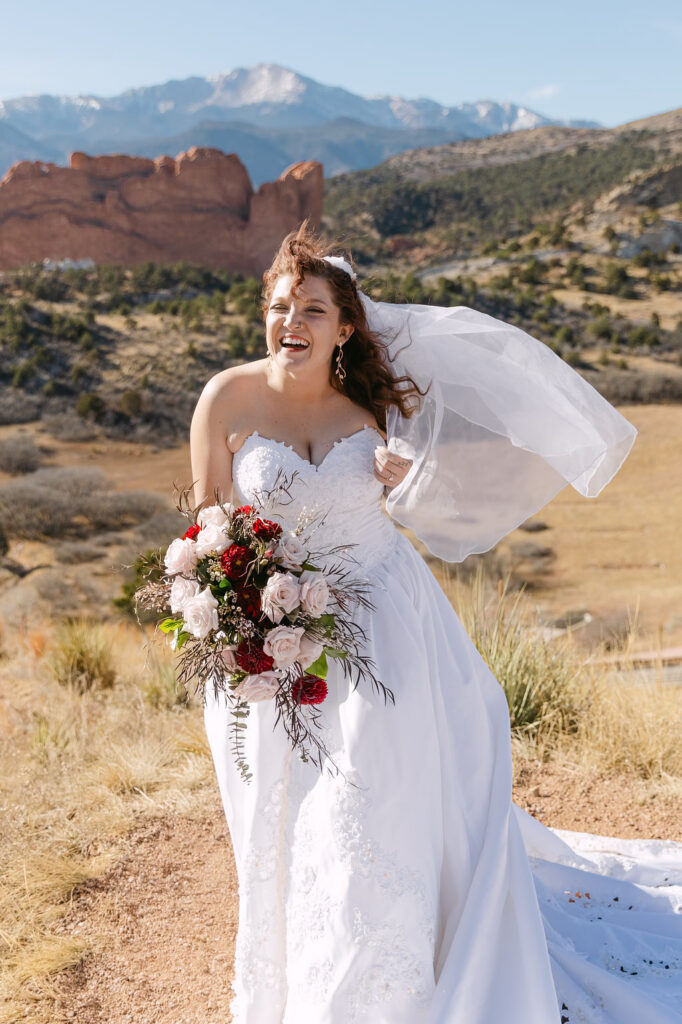 Natural wedding photo where the bride is laughing towards the camera as her veil blows in the wind captured by mrs ferree photography