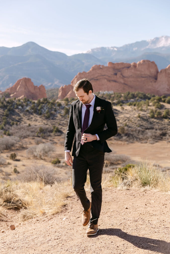 Groom walking through Garden of the gods buttoning his suit as he prepares for his wedding ceremony 