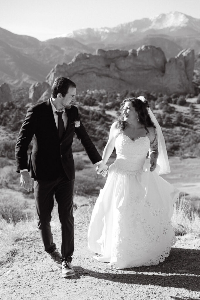 Black and white romantic wedding photo of bride and groom laughing as they hold hands in the sunshine in Garden of the gods