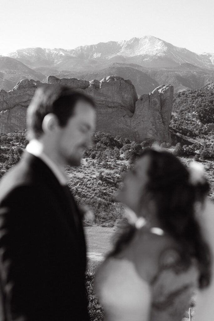 Artsy black and white photo of bride and groom standing in front of the mountains at garden of the gods with the mountains in focus during their wedding photos