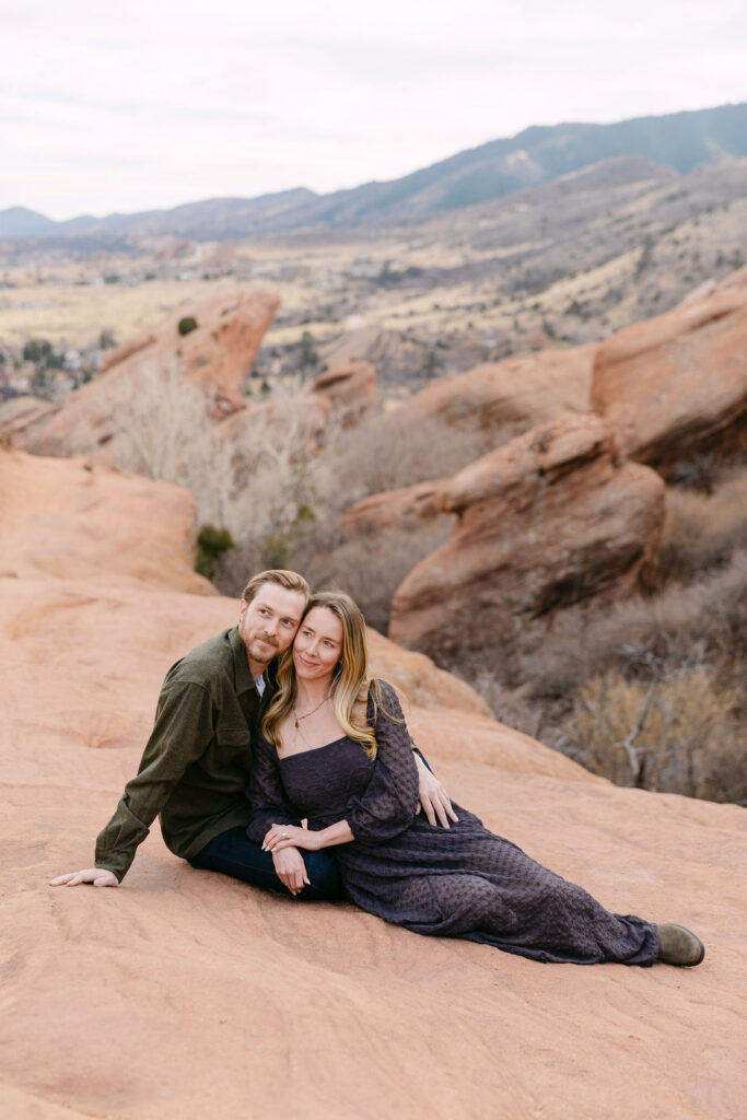 Editorial engagement photo of couple laying on red sandstone dramatically looking off into the distance 