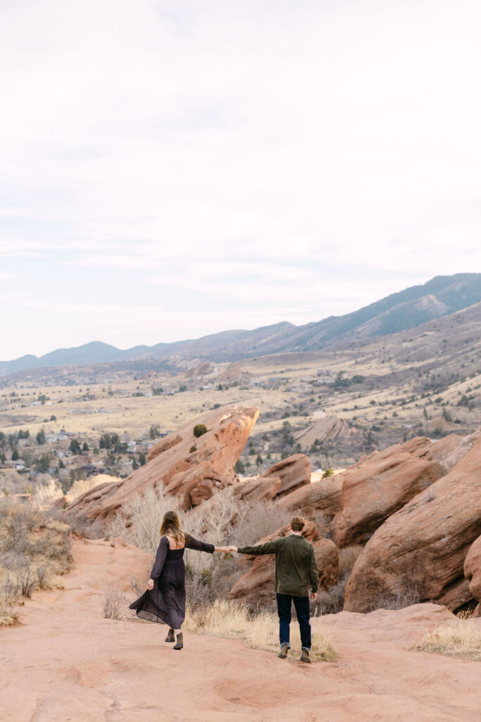 Wide scenery engagement photo of a couple wandering the Trading Post Trail at Red Rocks Park in Morrison, Colorado 