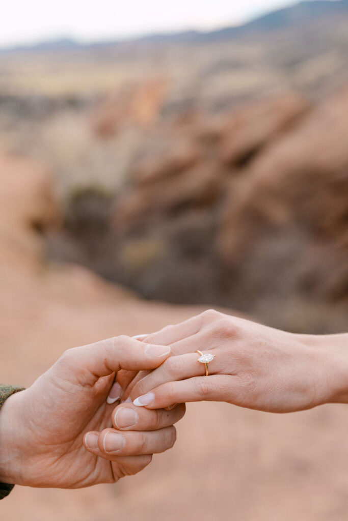 Up close photo of man holding his fiancee's hand with her solitaire gold ring highlighted against a mountain backdrop for Colorado engagement photos near Denver