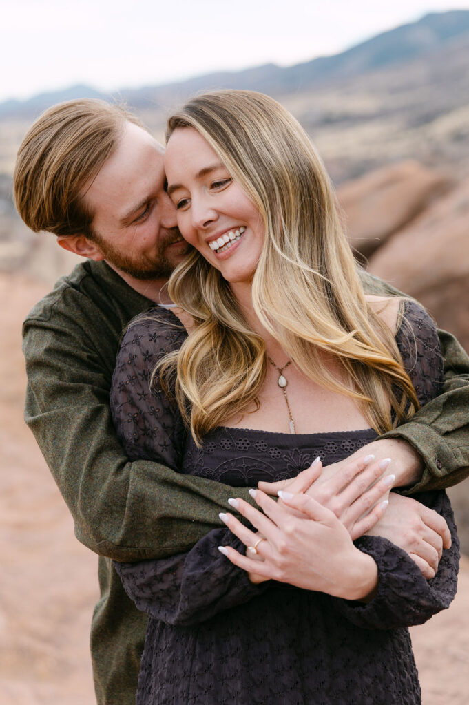 Cuddly, candid engagement photo of man wrapping his fiancee up in a hug while they laugh 