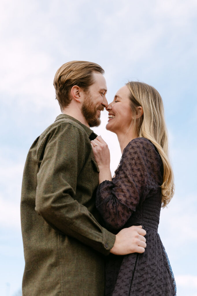 Couple cuddled up smiling big against the bright blue Colorado sky during their engagement photos 