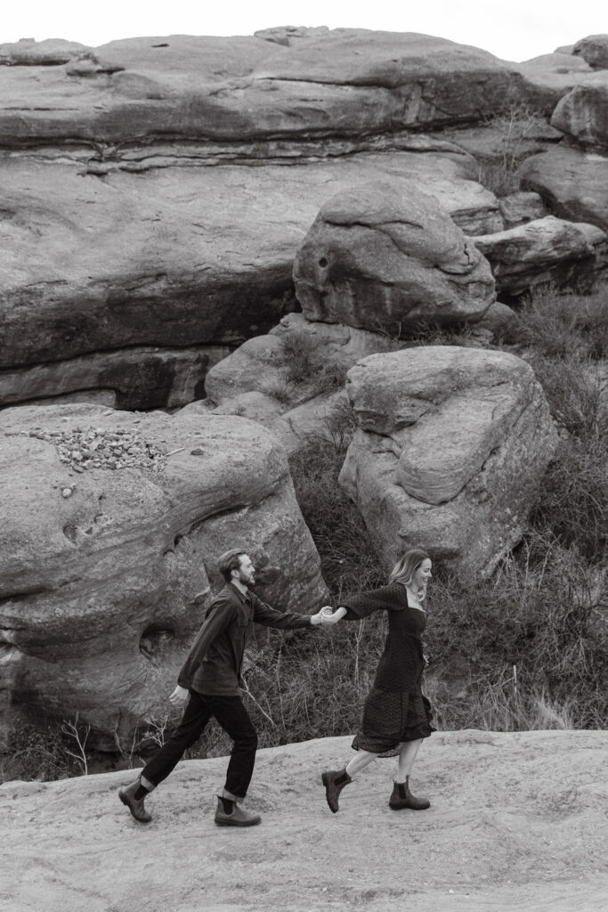 Artsy black and white engagement photo of a couple running quickly through a trail in Colorado at Red Rocks Park 