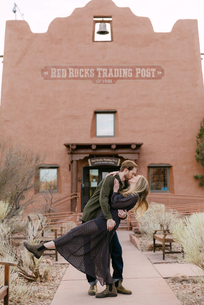 Couple doing a dip and kiss in front of the Red Rocks Trading Post for their Colorado engagement photos near Denver