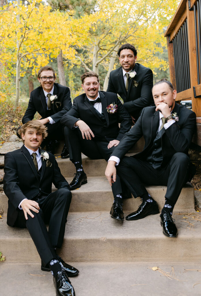 The groom sits with the wedding party on stone steps outside Wild Basin Lodge in Allenspark, Colorado, in Rocky Mountain National Park.