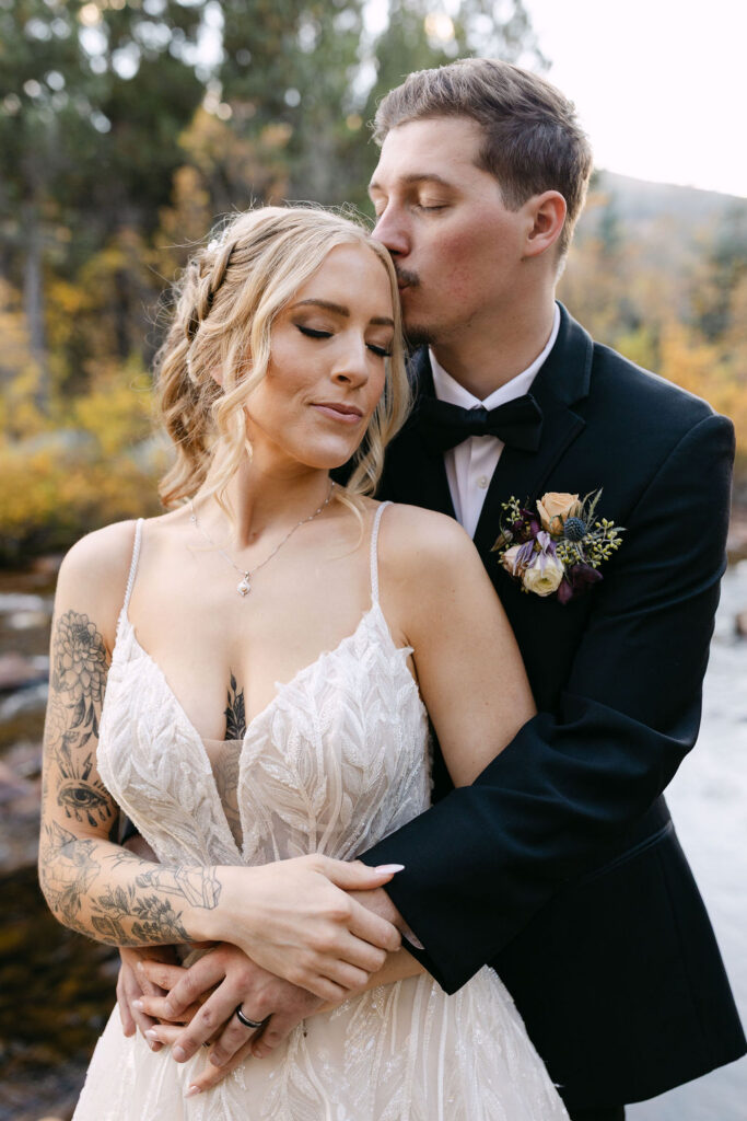 The couple embraces during portraits by a river at Wild Basin Lodge in Allenspark, Colorado, within Rocky Mountain National Park.
