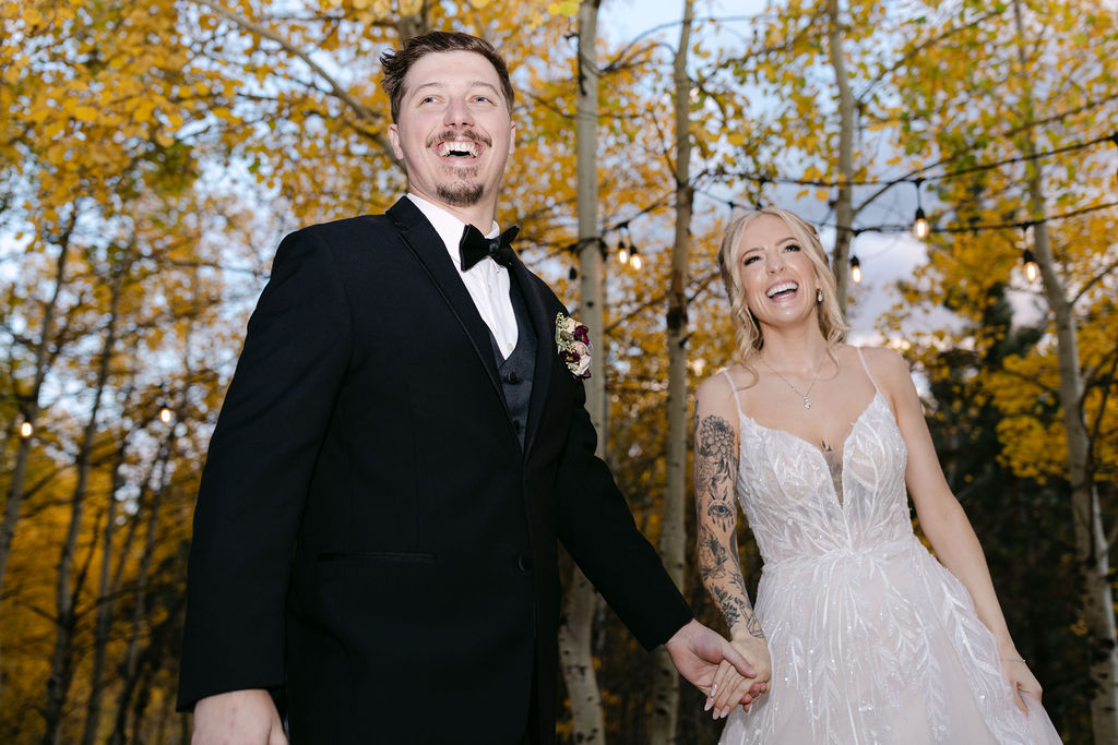 The couple holds hands and laughs beneath string lights outdoors at Wild Basin Lodge in Allenspark, Colorado, in Rocky Mountain National Park.