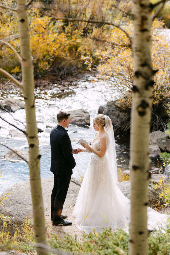 The couple stands facing each other during an intimate riverside ceremony at Wild Basin Lodge in Allenspark, Colorado, within Rocky Mountain National Park.