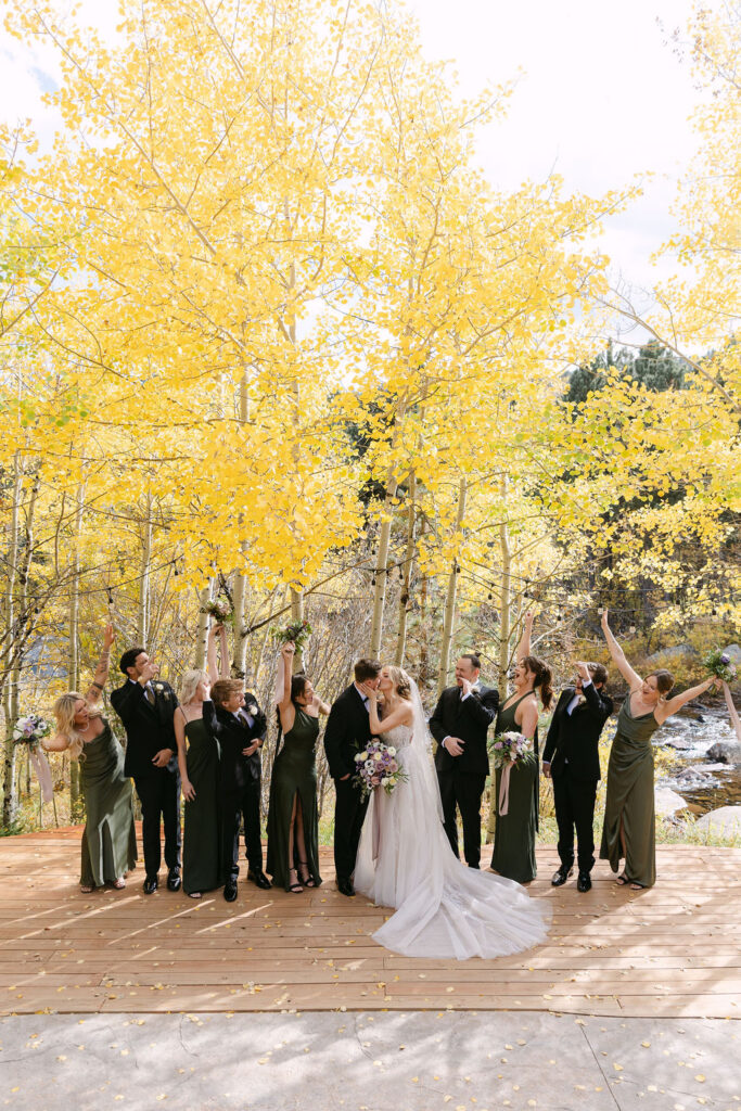 The wedding party celebrates beneath golden aspens on a wooden deck at Wild Basin Lodge.