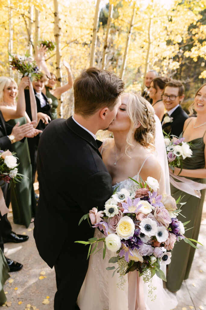 The couple shares a kiss as guests cheer beneath autumn aspens. 
