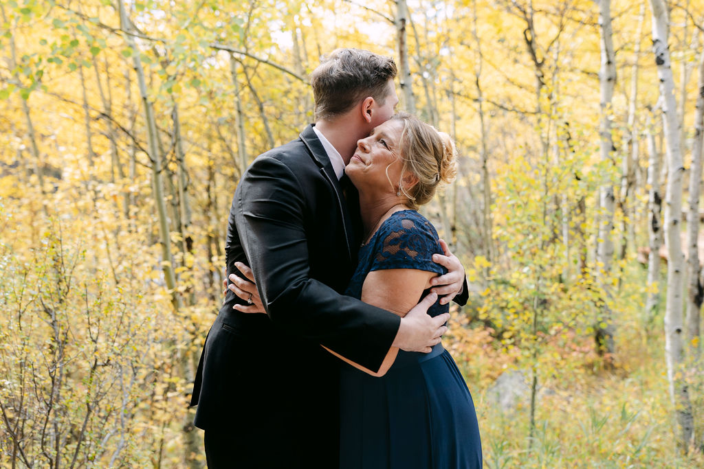 A groom embraces an older woman among fall aspens at Wild Basin Lodge in Allenspark, Colorado, inside Rocky Mountain National Park.