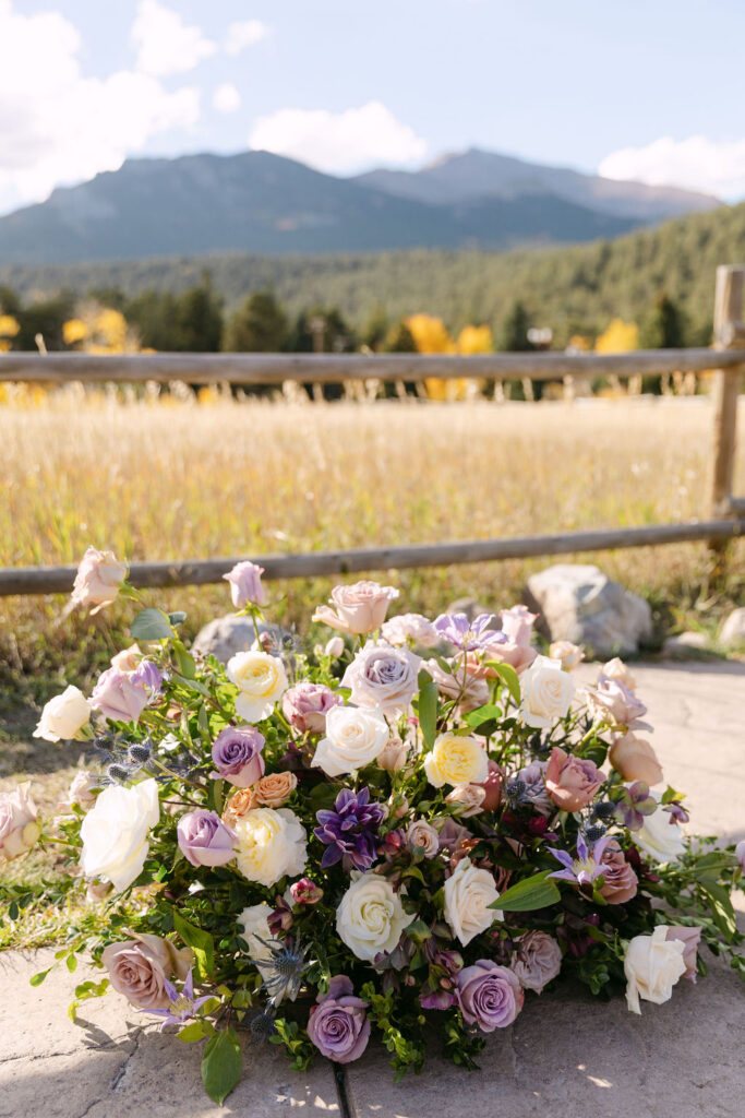 A low arrangement of pastel ceremony flowers sits beside a stone path at an outdoor mountain wedding in Colorado. 