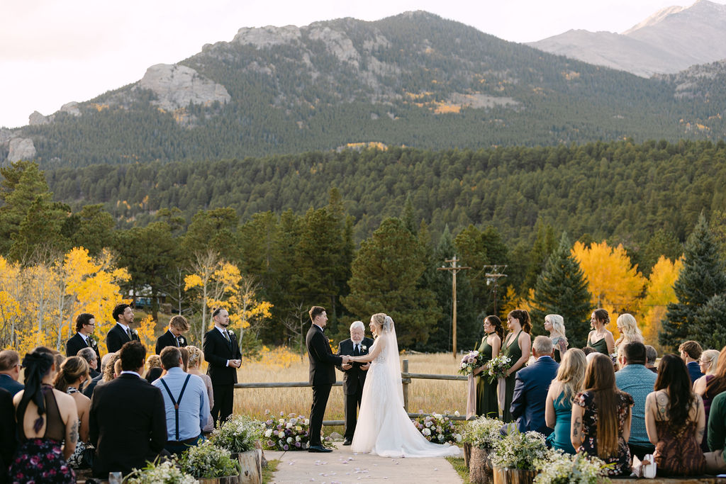 Wide view of a bride and groom holding hands during their fall mountain wedding ceremony in Colorado. 