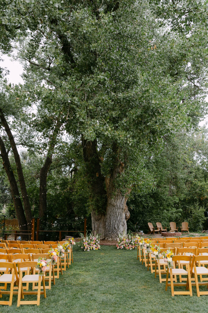 Garden ceremony site at the Lyons Farmette decorated with pink and yellow flowers and wooden chairs for an elevated backyard wedding feel