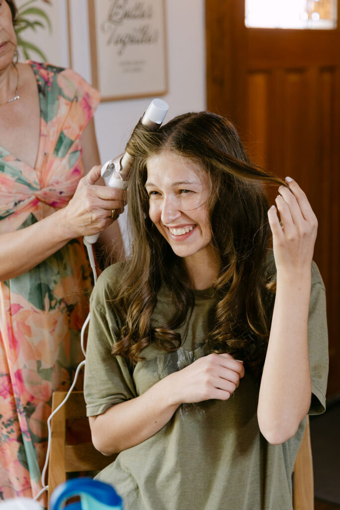 candid wedding photo of the bride smiling while her mom curls her hair before her outdoor colorado garden wedding